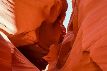 Narrow red rock canyon with smooth, curving walls and a glimpse of blue sky above.