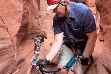 Person in red helmet and gear climbing narrow canyon with safety rope.
