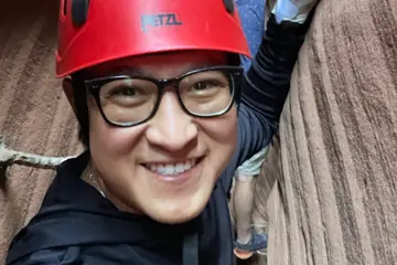 Two people in red helmets canyoning through narrow rock walls, one smiling at the camera.