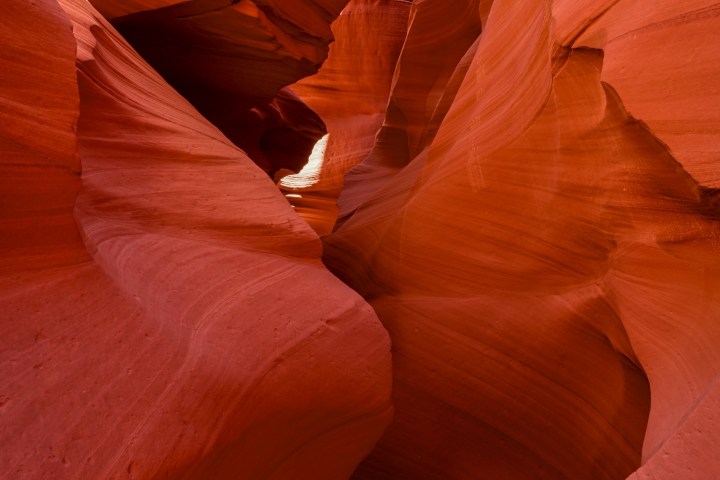 Narrow red rock canyon with smooth, curving walls and a glimpse of blue sky above.