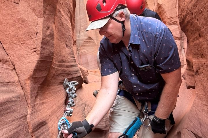 Person in red helmet and gear climbing narrow canyon with safety rope.