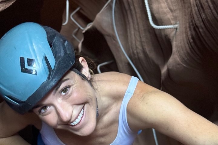 Person climbing a canyon wall with metal rungs and wearing a helmet, smiling upward.