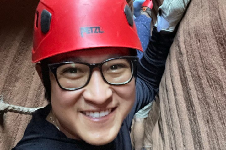 Two people in red helmets canyoning through narrow rock walls, one smiling at the camera.